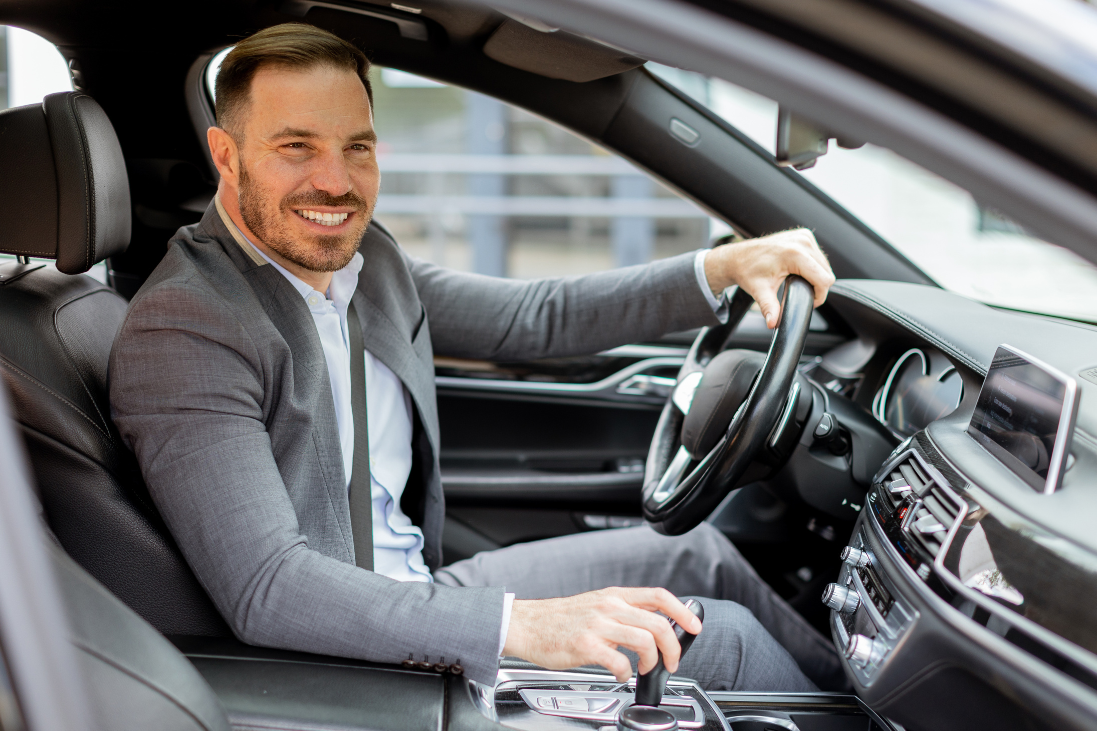 Smiling businessman driving luxurious car through city streets o